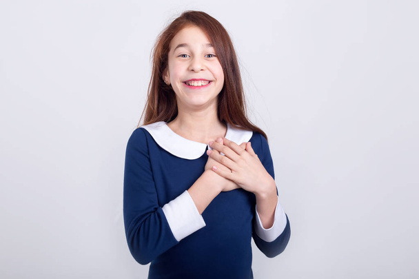 Happy girl holds hands on chest standing on a light background. Joyful schoolgirl. - 写真・画像
