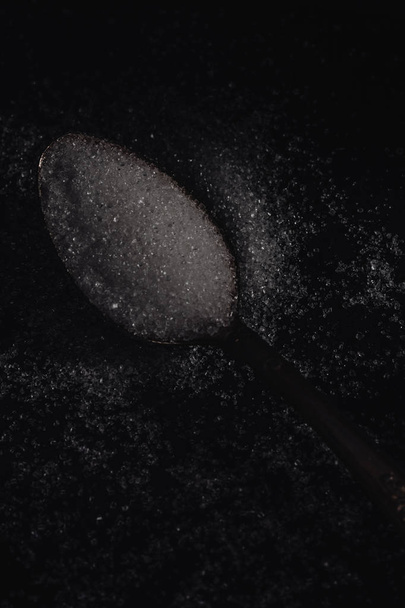 Dark photo of spoon with white sugar on the dark background, horizontal view, low key lighting - Photo, Image