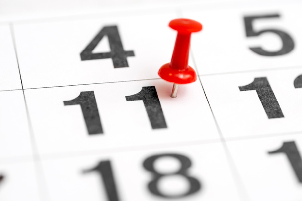 Pin auf der Datumsnummer 11. elfter Tag des Monats ist mit einer roten Daumennadel markiert. Anstecknadel im Kalender - Foto, Bild