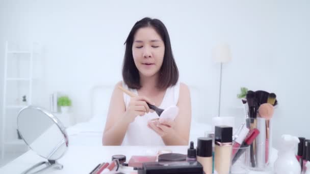 Beauty blogger present beauty cosmetics sitting in front camera for recording video. Happy beautiful young Asian woman use cosmetics review make up tutorial broadcast live video to social network. - Footage, Video