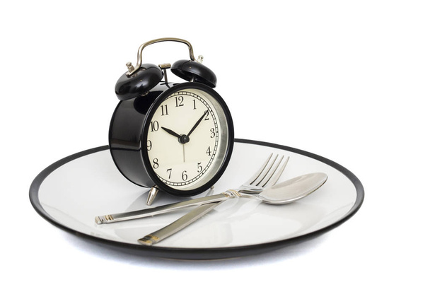 Reloj despertador negro con tenedor y cuchillo en la placa. Aislado sobre blanco. Hora de comer. Concepto de pérdida de peso o dieta
 - Foto, imagen