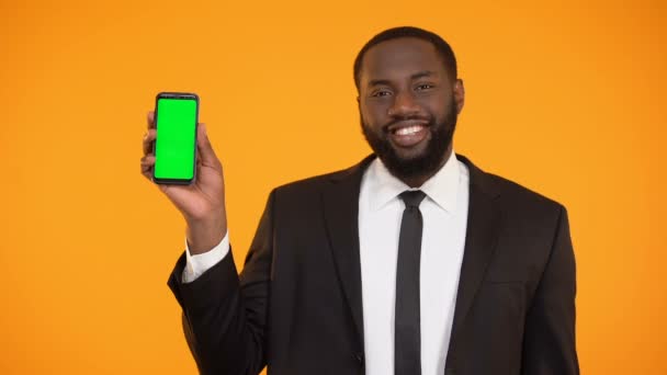 Smiling afro-american man in formalwear showing prekeyed phone, advertisement - Materiał filmowy, wideo