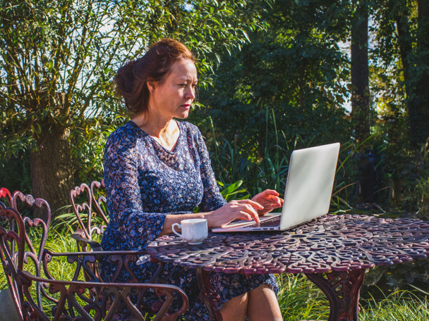 Vrouwelijke ondernemers van 50 jaar werken in de tuin met een laptop-co - Foto, afbeelding