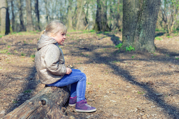 Sevimli küçük beyaz sarışın kız sittng ahşap oturum orman ve bir yerde arıyor. Çok güzel dalgın çocuk hakkında bir şey park veya orman yürüyüş sırasında rüya - Fotoğraf, Görsel
