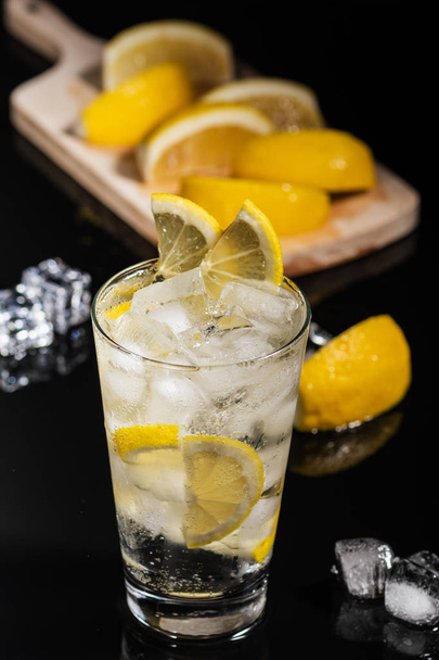 Gim tônico com fatias de limão e cubo de gelo, com limão e gelo para decorar nas costas, no fundo preto
 - Foto, Imagem