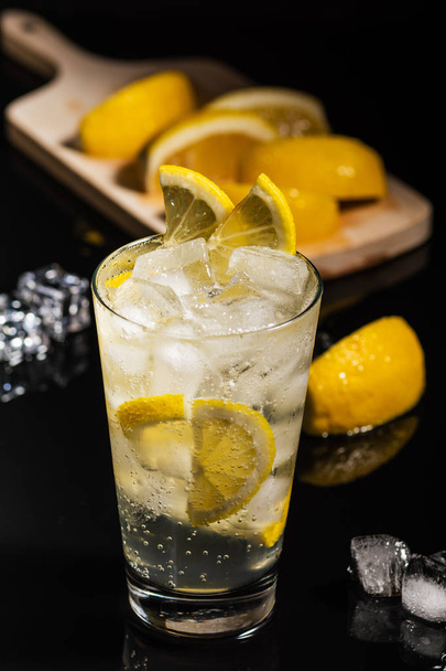 Gin Tonic mit Zitronenscheiben und Eiswürfel, mit Zitrone und Eis zum Dekorieren auf dem Rücken, auf schwarzem Hintergrund - Foto, Bild