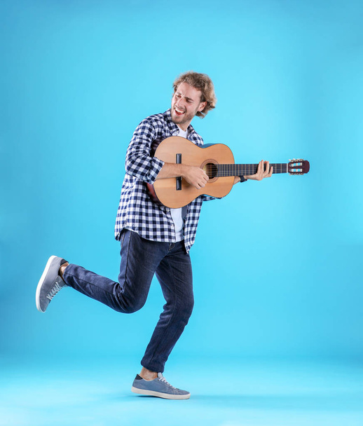 Young man playing acoustic guitar on color background - Фото, изображение