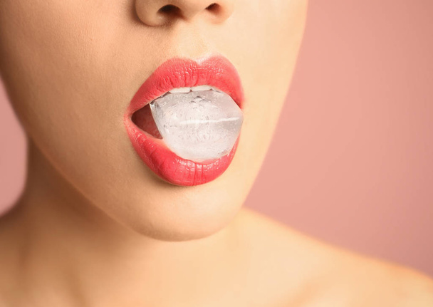 Young woman holding ice cube in mouth on color background, closeup - Foto, imagen