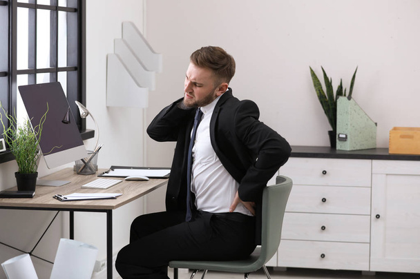 Businessman suffering from back pain at workplace - Foto, Imagen