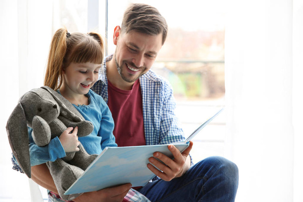 Felice uomo e la sua piccola figlia leggere libro vicino alla finestra a casa
 - Foto, immagini