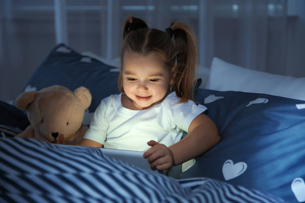 Beautiful little girl with gadget and toy in bed at night. Bedtime schedule - Fotoğraf, Görsel