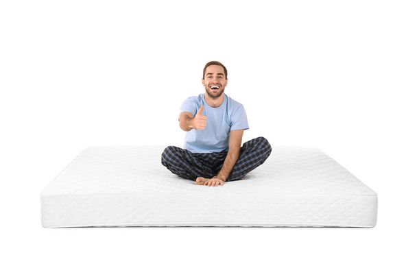Young man sitting on mattress against white background - 写真・画像