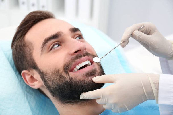 Dentist examining young man's teeth with mirror in hospital - Fotografie, Obrázek