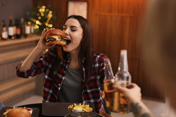 Young woman eating tasty burger in cafe - Foto, Imagem