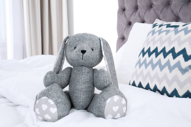 Cute toy rabbit sitting on bed indoors - Foto, imagen
