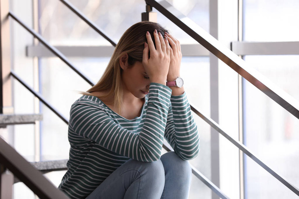 Emotional teenage girl sitting on stairs indoors - Foto, afbeelding