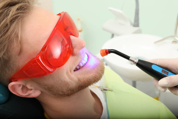 Young patient undergoing teeth whitening procedure in clinic. Visit dentist - Foto, afbeelding