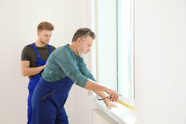 Service men measuring window for installation indoors - Foto, immagini