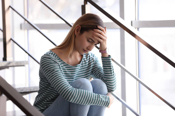 Emotional teenage girl sitting on stairs indoors - Photo, image