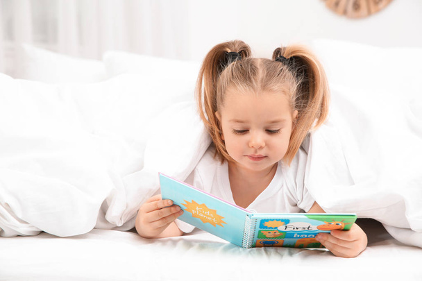 Beautiful little girl with book in bed at home. Bedtime schedule - Fotó, kép