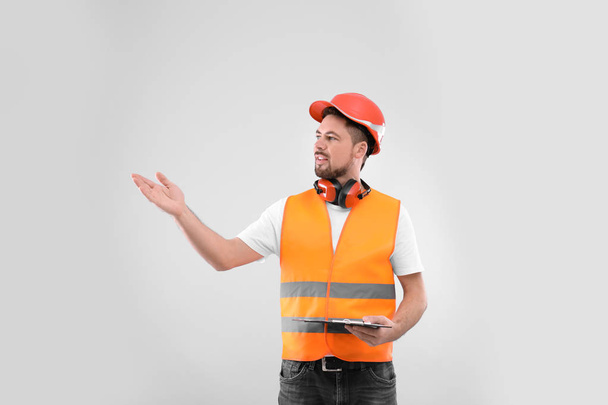 Male industrial engineer in uniform with clipboard on light background. Safety equipment - Foto, afbeelding