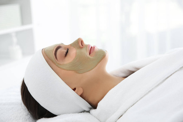 Pretty woman with clay mask on her face in spa salon - Photo, Image