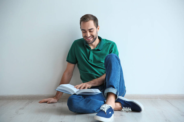 Young man reading book on floor near wall - Zdjęcie, obraz