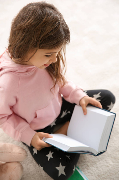 Cute little girl reading book on floor at home - Foto, Bild