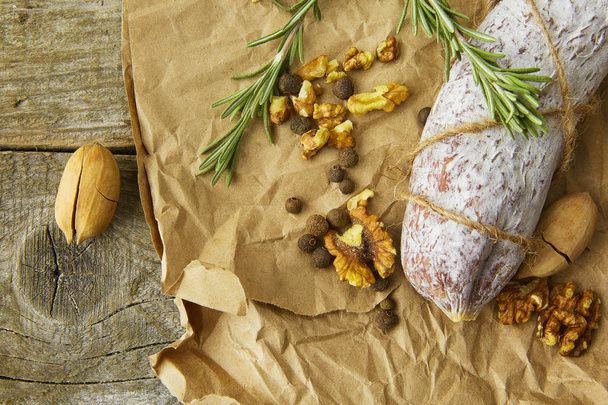 Italian salami wih sea salt, rosemary, garlic and nuts on paper. Rustic style. Top view. - Foto, imagen