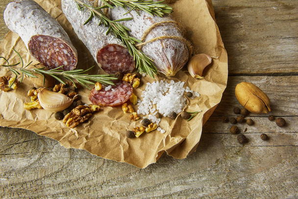 Italian salami wih sea salt, rosemary, garlic and nuts on paper. Rustic style. Close up. - 写真・画像