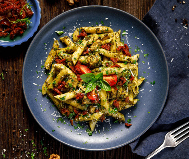 Penne pasta met spinazie, zongedroogde tomaten en kip, besprenkeld met Parmezaanse kaas en verse peterselie op een keramische plaat, bovenaanzicht. - Foto, afbeelding