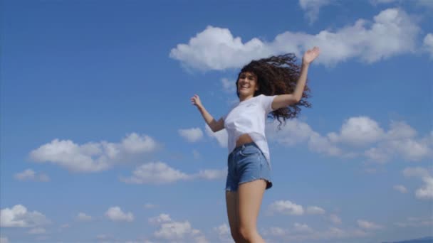 Szczęśliwa młoda kobieta z pięknymi kręconymi włosami skacząc, niebieskie tło nieba, 4k 75 fps slow motion - Materiał filmowy, wideo