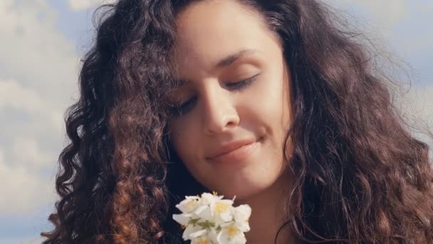 Mooie Kaukasische jonge vrouw met krullend haar ruikende bloem, 4k 75 fps slow motion - Video