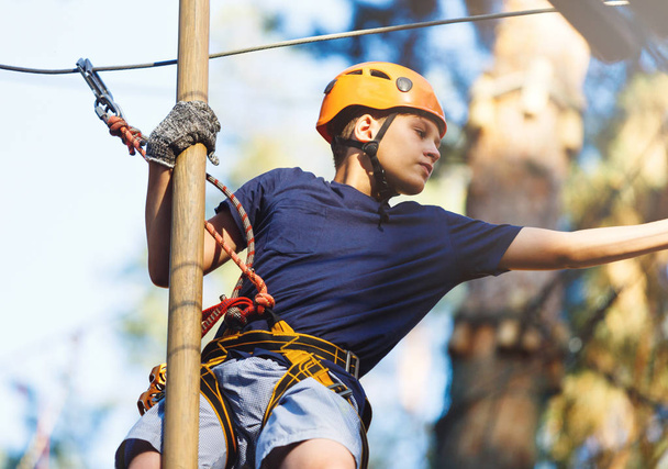 Sporty, young, cute boy in white t shirt spends his time in adventure rope park in helmet and safe equipment in the park in the summer. Active lifestyle concept - Foto, Imagen