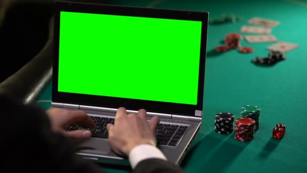 Male gambler betting poker online on laptop, holding lucky dice, green screen - Кадры, видео