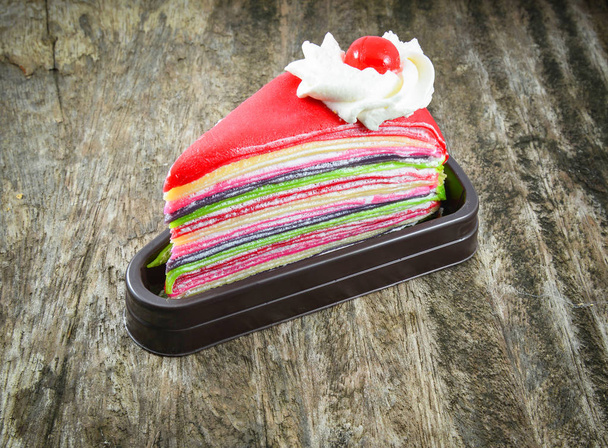 Gâteau de colza arc-en-ciel coloré à la crème et cerise rouge sur le vieux woo
 - Photo, image