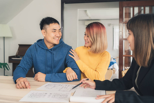 Happy young Asian couple and realtor agent. Cheerful young man signing some documents while sitting at desk together with his wife. Buying new house real estate. Signing good condition contract. - Photo, Image