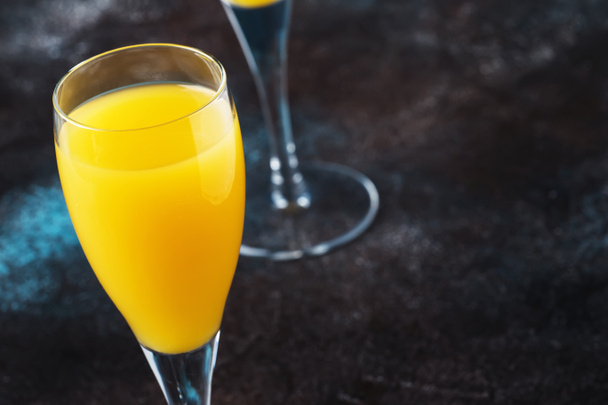 Low alcohol cocktail mimosa with orange juice and cold dry champagne or sparkling wine in glasses, blue background with flowers, place for text, selective focus - Фото, зображення