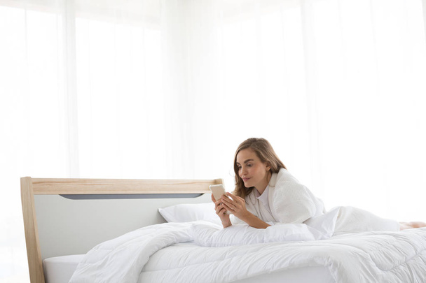 Relaxado mulher caucasiana usando um smartphone de manhã na cama no quarto em casa
 - Foto, Imagem
