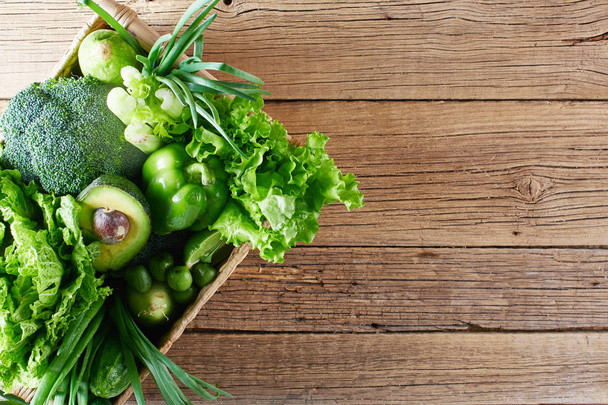 Green vegetables and fruits and greens in a brown wicker basket on a wooden background. Healthy eating concept - Foto, immagini
