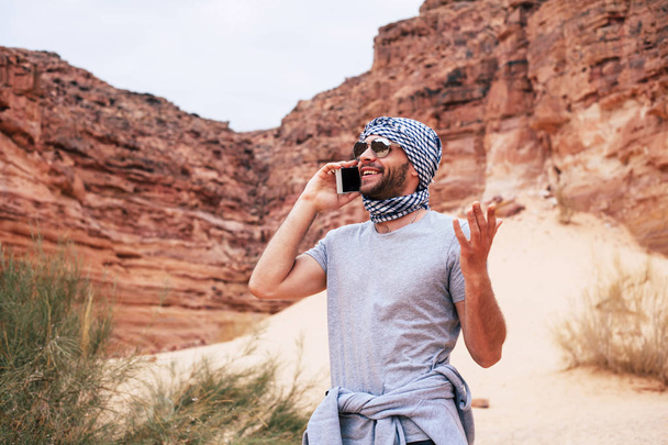 traveller wearing keffiyeh and sunglasses talking on phone in desert scene - Foto, Imagen