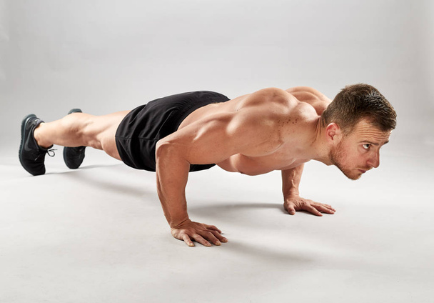 Fitness model doing pushups on gray background in studio - Foto, Imagem