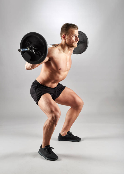 Man doing squats with barbell on neck back, studio shot - Foto, immagini