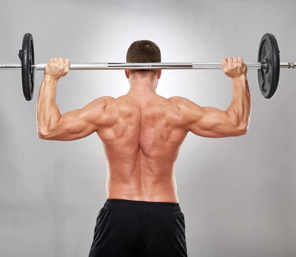 Man doing shoulder workout with barbell on gray background - Φωτογραφία, εικόνα