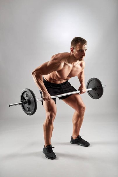 Man doing back workout, barbell row in studio over gray background - Foto, afbeelding