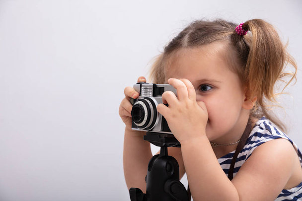 Little Girl Standing Against White Background While Taking Picture Using Photo Camera - Valokuva, kuva