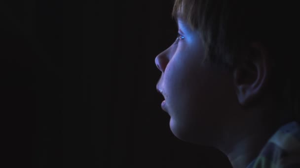 Young boy watching cartoons in a dark room on a computer - Materiał filmowy, wideo