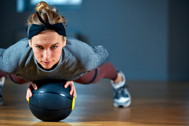 Fit and muscular woman with piercing eyes doing intense core workout with kettlebell in gym. Female exercising at crossfit gym. - Photo, Image
