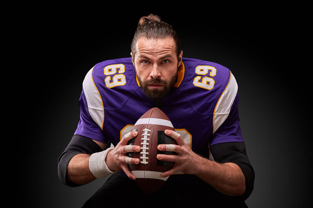 Πορτρέτο του αμερικανικού ποδοσφαίρου παίκτης που κρατάει μια μπάλα με τα δύο του χέρια - Φωτογραφία, εικόνα