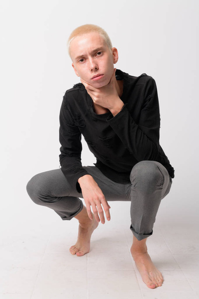Full body shot of young androgynous man crouching and looking at camera - Foto, immagini